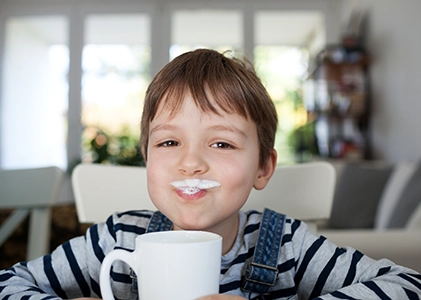 Niño bebiendo leche con bigote de leche en vaso
